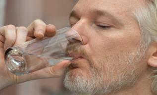 Assange bebe agua durante la rueda de prensa.