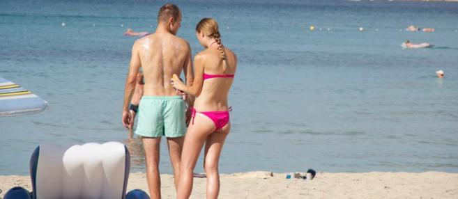 Dos bañistas se aplican protector solar en una playa.