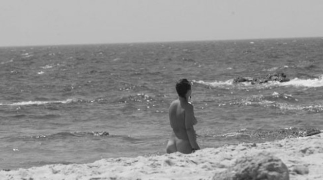 Una nudista pasea por una playa.