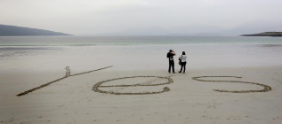 Una pareja escribe su postura en la arena.