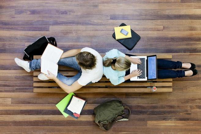 Universitarios españoles, estudiando con un libro y un portátil.