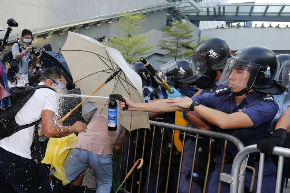 Un antidisturbios echa gas pimienta a un manifestante pro democracia,...