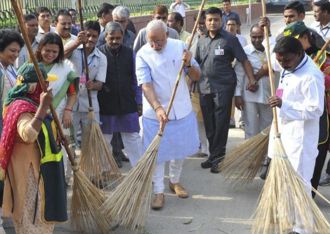 El primer ministro indio, Narendra Modi (centro), limpia las calles...