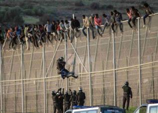 Un guardia civil forcejea con un inmigrante encaramado a la valla de...