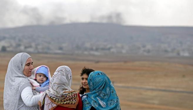 En segundo plano, columnas de humo salen de la ciudad kurdo siria de...