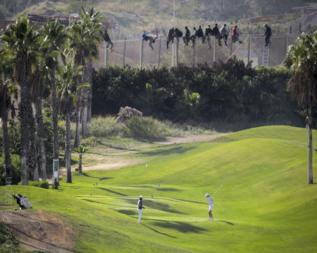 Personas jugando al golf con los inmigrantes encaramados en la valla.