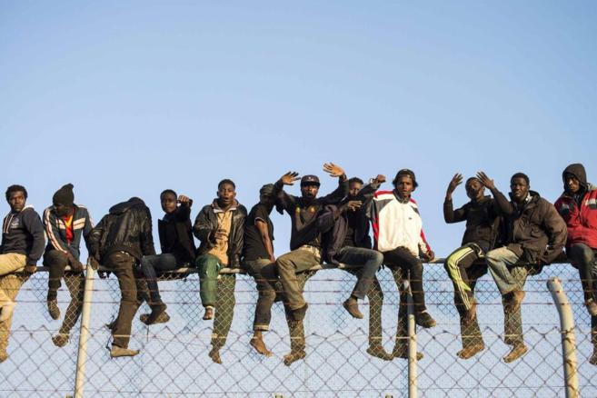 Inmigrantes subsaharianos subidos a lo alto de la valla en el intento...
