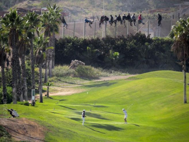 Dos mujeres juegan al golf mientras varios inmigrantes permanecen...