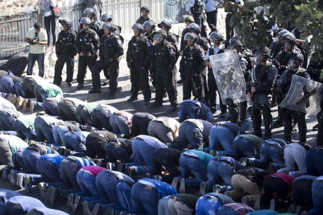 Policas israeles vigilan a un grupo de palestinos que rezan cerca...