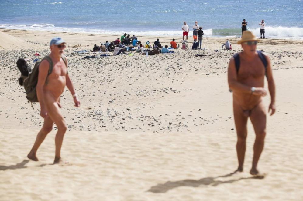 Dos turistas nudistas pasean por la playa de Maspalomas. Detrs se...