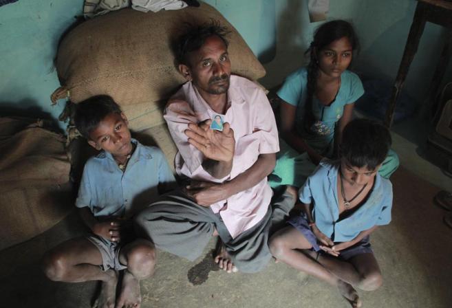Un padre indio rodeado de sus hijos muestra una foto de su mujer,...