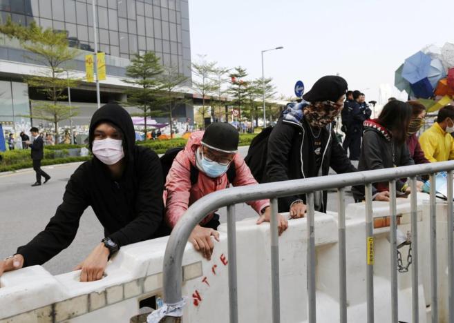 Varios manifestantes con la cara cubierta ayudan a la retirada de...