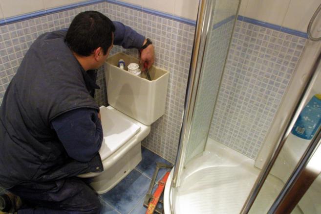 Un operario realiza una reparacin en la cisterna del inodoro de una...