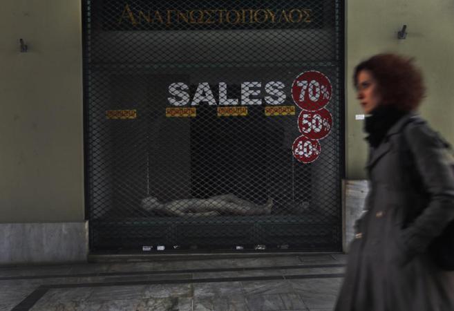 Una mujer griega pasea por delante de una tienda de ropa cerrada por...