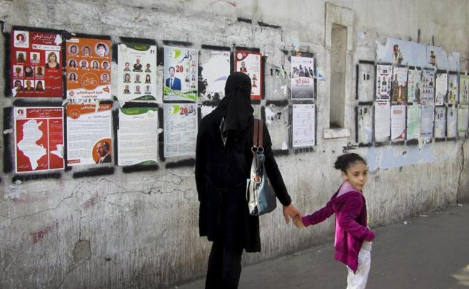Una mujer y su hija pasan junto a carteles electorales desplegados en...