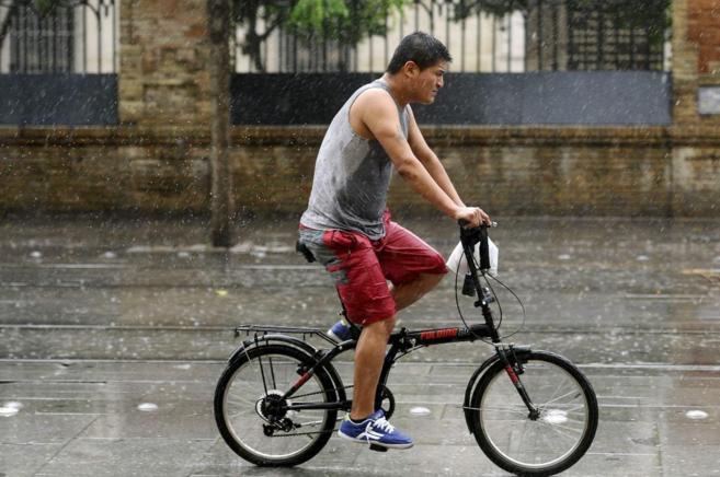 Un hombre pasea en bicicleta por Sevilla bajo la lluvia.
