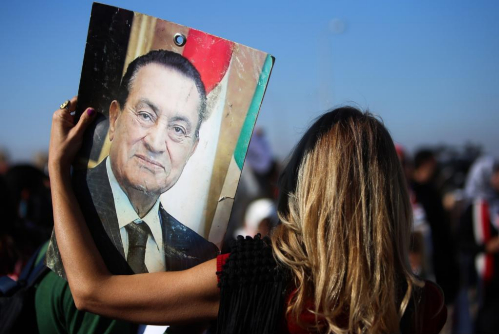 Una mujer sostiene una pancarta con la cara de Mubarak  a las puertas...