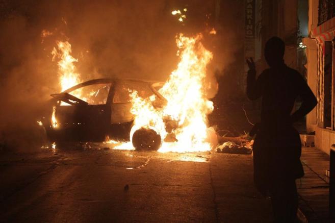 Un hombre pasa junto a un coche incendiado en Atenas.