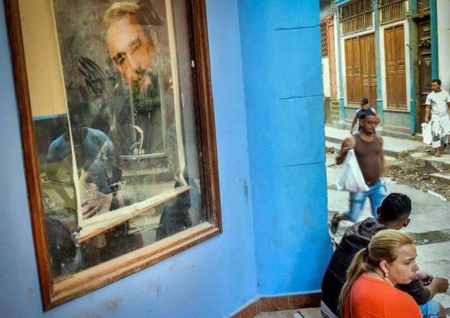 Cubanos sentados junto a un poster de Fidel Castro en La Habana.