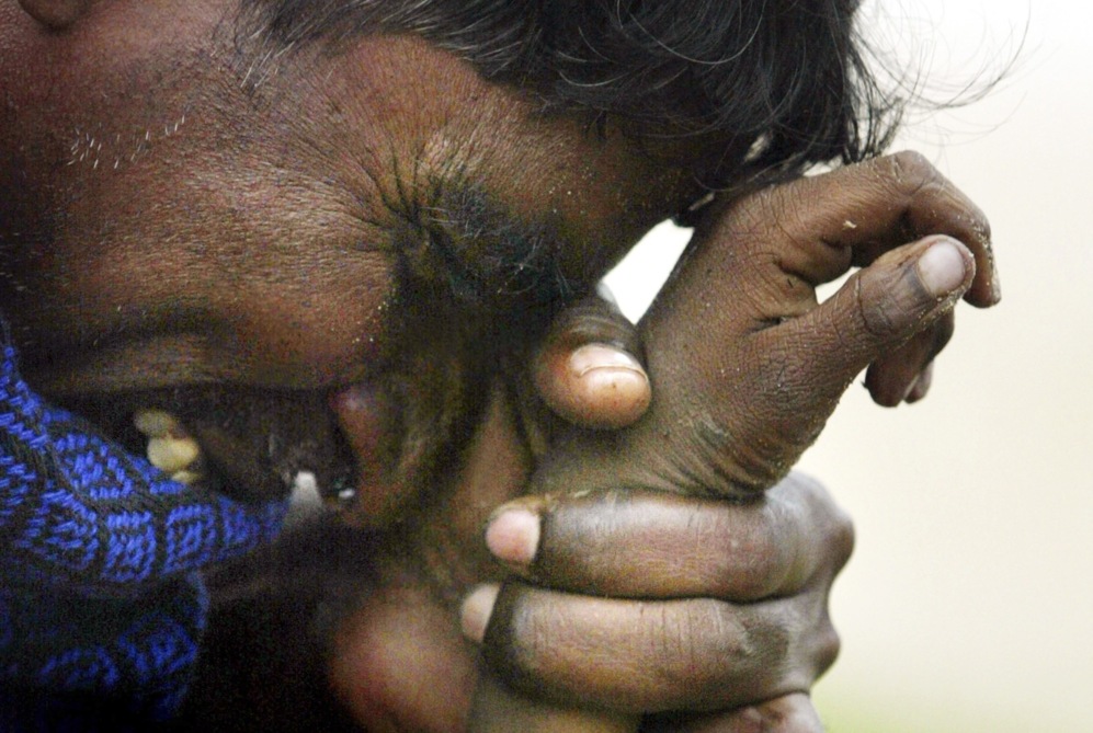 Un hombre indio llora mientras sostiene la mano de su hijo de...