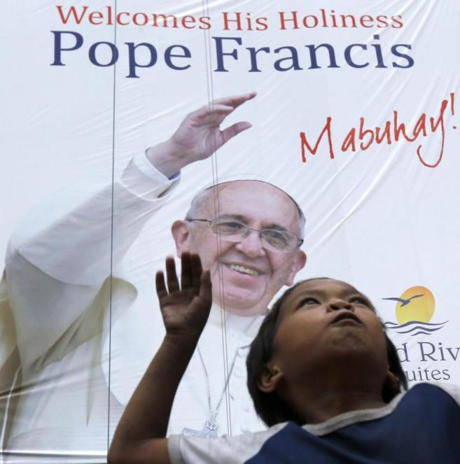 Una nia filipina bajo un cartel de bienvenida al Papa.