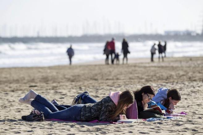 Una mujer y sus hijas leen tumbadas en la playa de Las Arenas,...