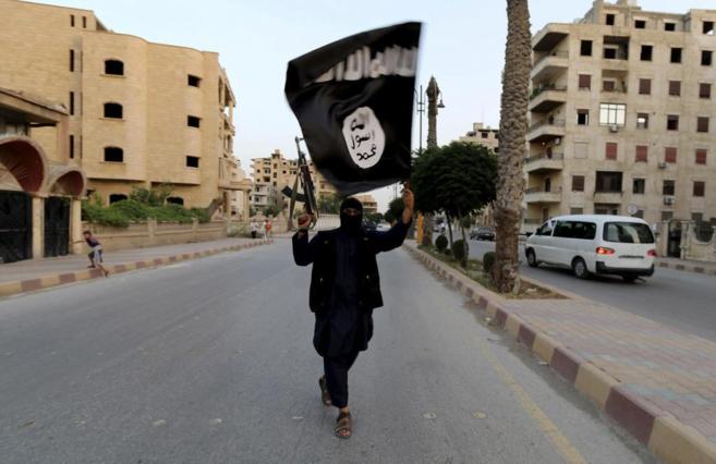 Un partidario del Estado Islámico, armado y alzando la bandera que...