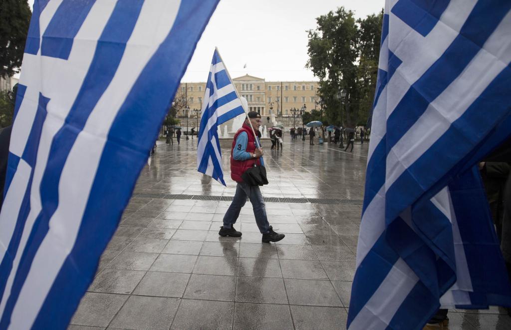 Un hombre pasea por la plaza de Syntagma, en Atenas, con una bandera...
