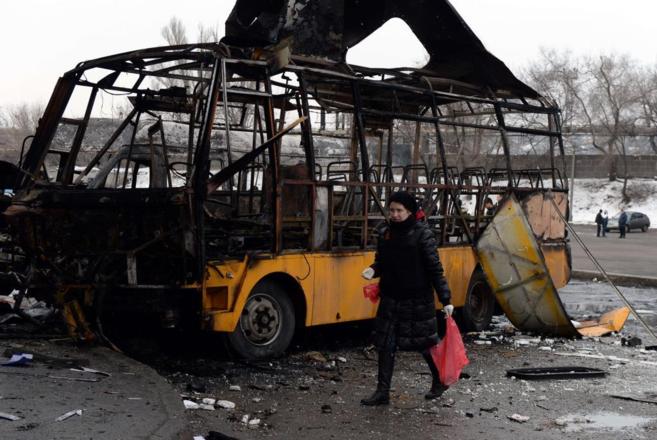 Una civil ucraniana pasa junto a uno de los autobuses alcanzados por...