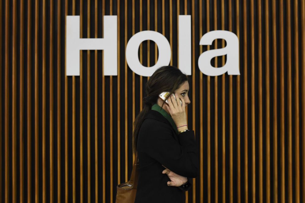 Una mujer usa su telefono junto a un cartel de bienvenida.