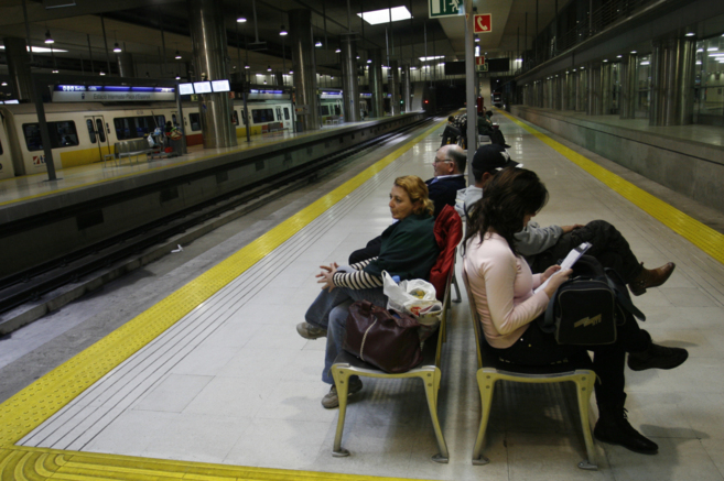 Varios pasajeros esperando el metro en unos bancos de la Estacin...