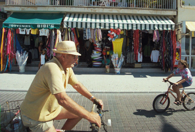 Un hombre y una nia pasean en bici frente a dos tiendas de...
