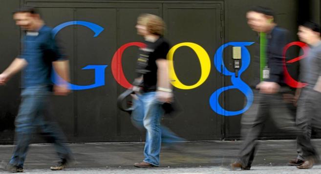 Personas caminan pro delante de un logo de la tecnológica Google.
