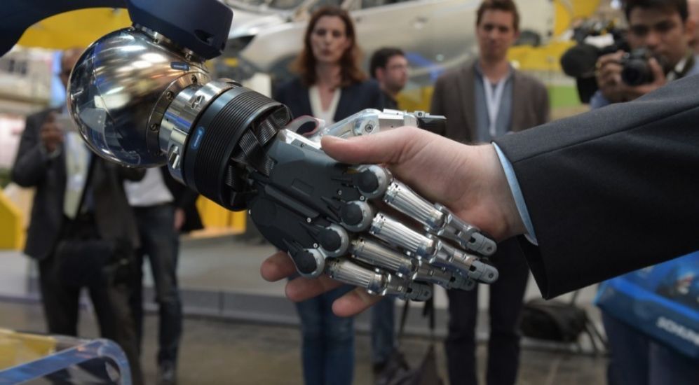 Un visitante le da la mano a un robot en la feria Hannover Messe.