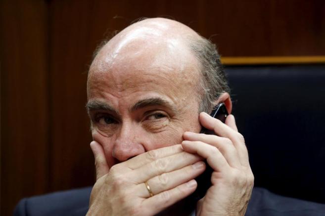 El ministro de Economía, Luis de Guindos, se tapa la boca mientras...