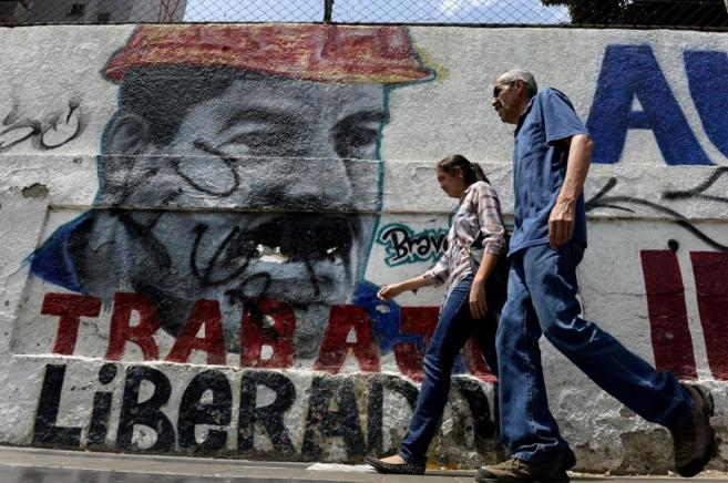 Dos venezolanos caminan junto a un grafiti del presidente Maduro en...