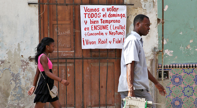 Dos cubanos pasan junto a un cartel animando al voto, ayer, en La...