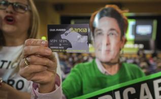 Una mujer con una careta del presidente de Bankia sostiene una tarjeta...
