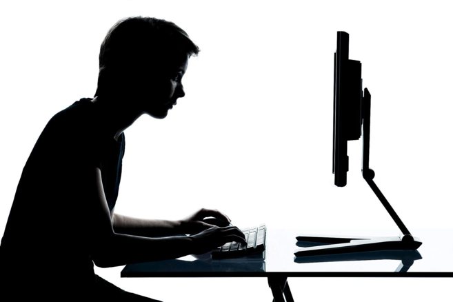 Un joven, de perfil, tecleando en un ordenador.