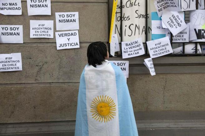 Un joven ataviado con la bandera argentina mira varios carteles que...