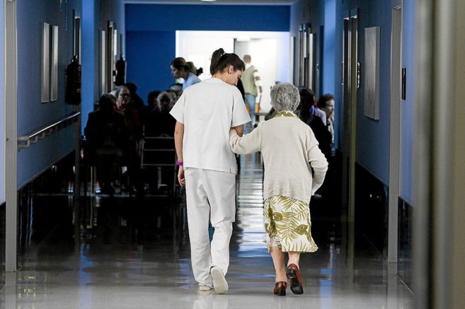 Una auxiliar ayuda a una mujer anciana a caminar por el interior de...