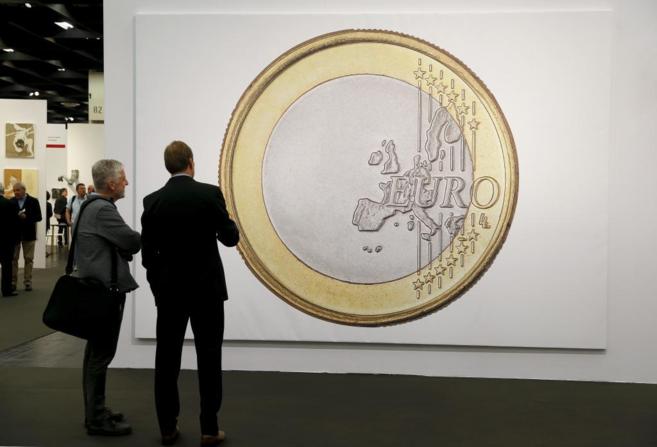 Dos personas observan una foto de una moneda de euro, cuyo uso mermar...