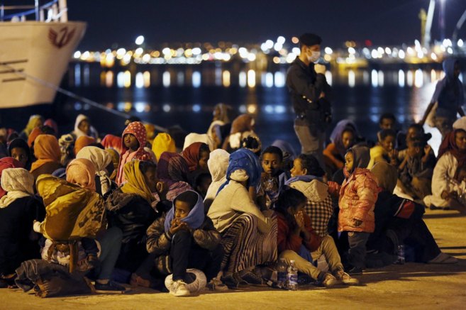 Unos migrantes descansan tras desembarcar en el puerto siciliano de...