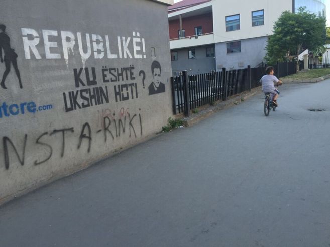 Un nio recorre en bici una calle de Prstina, junto a un grafiti...