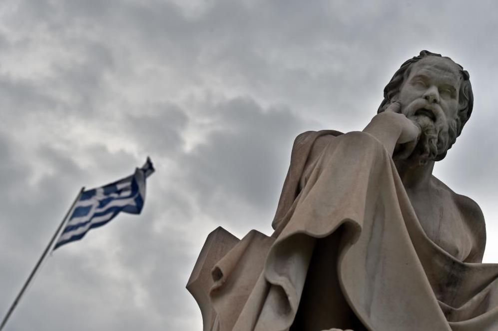 La bandera griega ondea junto a una estatua del filsofo griego...