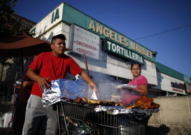 Dos latinos preparan comida en un puesto callejero de Los ngeles.