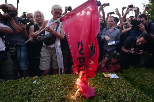 Una mujer quema una bandera del partido Syriza, tras la claudicacin...