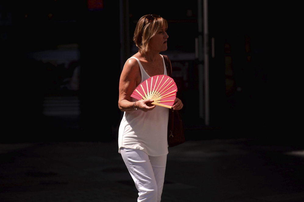 Una mujer se abanica en una tarde de calor sofocante en el centro de...