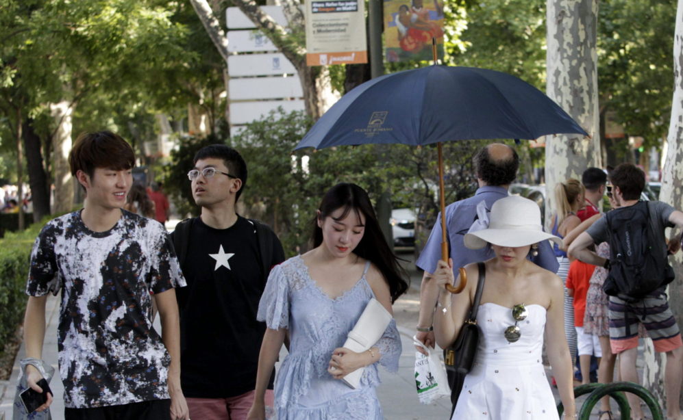 Unas turistas tratan de protegerse del sol con sombreros, paraguas y...