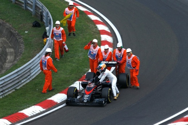 Fernando Alonso empujando su monoplaza con ayuda de los comisarios.